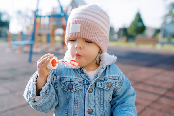 istock Little girl blowing soap bubbles on a sunny playground 2155911234