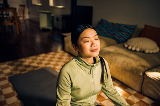 young asian woman meditating in living room. indoor lifestyle portrait. self-care and mindfulness concept. - zen imagens e fotografias de stock