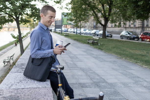 istock Smiling businessman commuter using mobile phone. He is enjoying at public park on his bicycle trip from work after a long workday. Sustainable concept of going to work by bicycle. 2155923842
