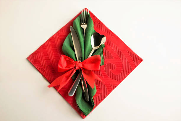 Top view of green and red christmas napkin elegantly folded with cutlery set on white surface with copy space