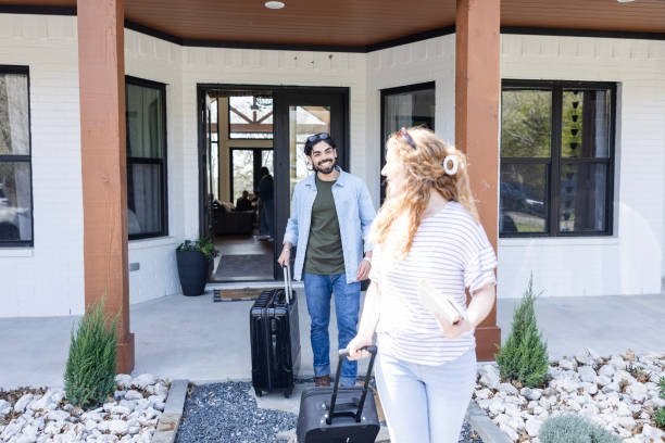 istock Wheeling suitcases out, young woman looks back at husband 2155928052