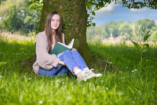 istock Teenage girl sitting under a tree reading 2155933641