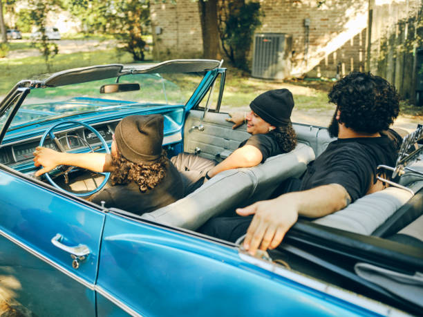 Three young hispanic men in a lowrider convertible vintage car, driving out of the garage driveway.