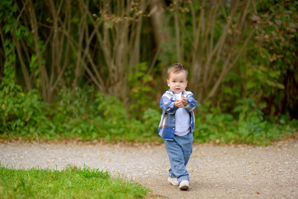 A cute baby boy is playing with pebbles on a park path on a summer day. Sensory development of little kids. Keen toddler having fun outdoor.