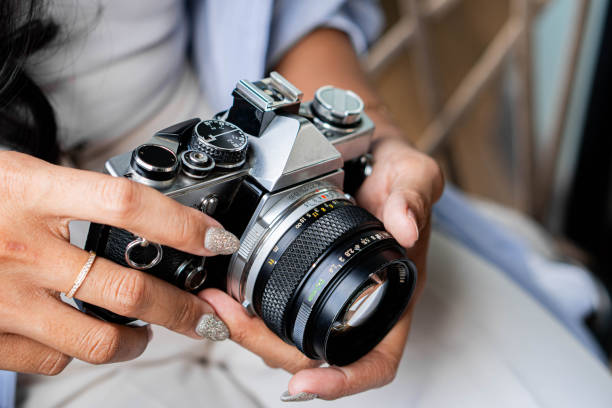 Close-up of a person holding a vintage film camera, focusing on the camera's details and the person's hands with manicured nails.