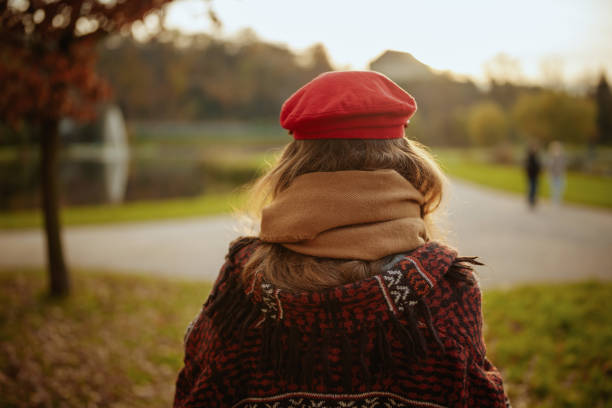 Hello autumn. Seen from behind woman in red hat with scarf walking in the city park.