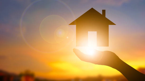 istock Silhouette hand holding home icon sunset blur background 2155962062