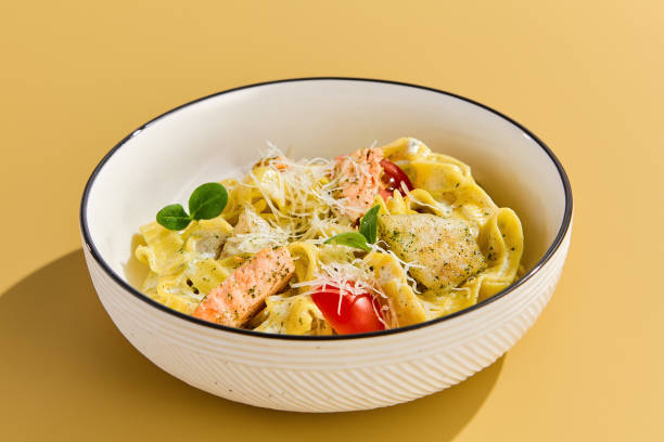 Delicious Homemade Pasta with Salmon and Tomatoes on Yellow Background