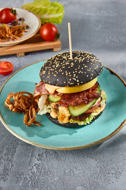 istock Gourmet black burger with bacon and crispy onions on a turquoise plate, gray textured backdrop with a hint of sunlight 2155972026
