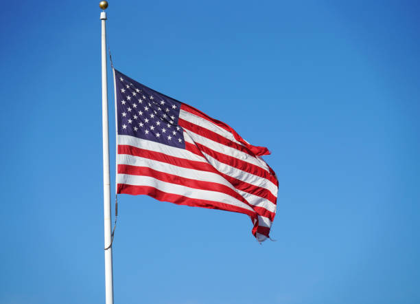 istock waving USA flag on pole against blue sky 2155972388