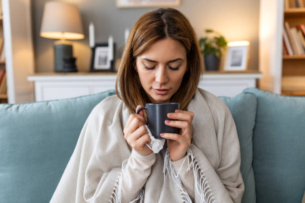 istock Sickness, seasonal virus problem concept. Woman being sick having flu drinking tea on sofa. Sick woman lying in bed with high fever. Cold flu and migraine. 2155975660