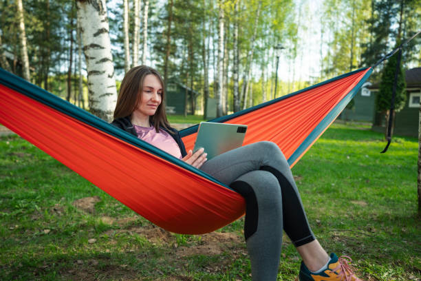 istock Positive woman sits in a hammock outdoors and uses digital tablet 2155977133
