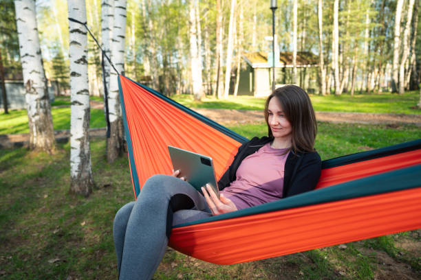 istock Positive woman sits in a hammock outdoors and uses digital tablet 2155977180