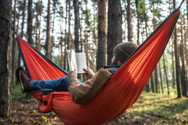istock A man reading a book in hammock in the woods 2155977706