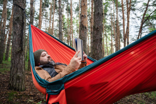 istock A man reading a book in hammock in the woods 2155977759