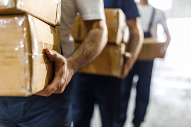 istock Close up of unrecognizable workers carrying carton boxes in a storage room. 2155978688