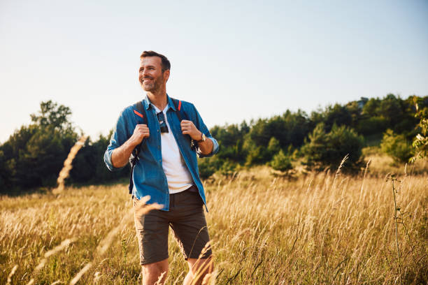 Handsome adult man hiking through meadow with backpack