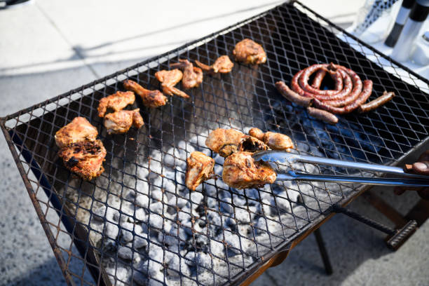 Chicken pieces and sausage on a home made coal fired barbecue grill with barbecue tongs