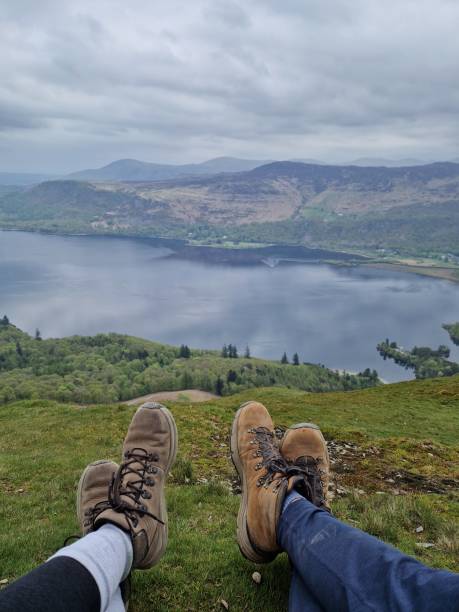 Close Up Shot of Two Pairs of Hiker Legs in Hiking Boots on a Mountain over the Lake in Background. Lake District National Park, UK. Close Up Shot of Two Pairs of Hiker Legs - Female and Male - in Hiking Boots, sitting on the Ground on a Mountain over the Lake in the Background. Lake District National Park, England, UK. brown leg stock pictures, royalty-free photos & images