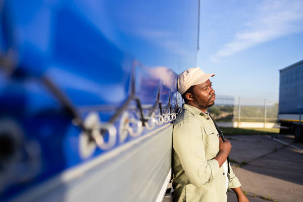 A mature African-American man wearing a reflective vest and carrying a hardhat and backpack, standing at a bus stop.