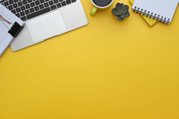 istock Top view of laptop, notepad, coffee cup and financial documents on yellow background 2155987706