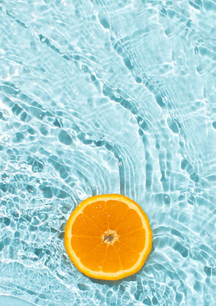 istock Orange fruit slice flowing on blue rippled water background. Summer fruity concept. 2155988268