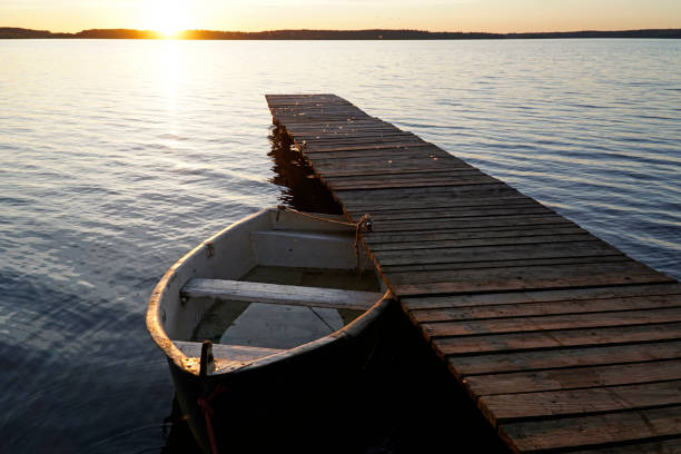 Old white boat and wooden footbridge on lake shore at sunset - Masuria, Poland.