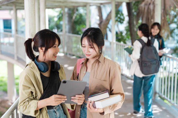 istock asian student socializing with tablet and books on campus walkway. university concept 2155993386