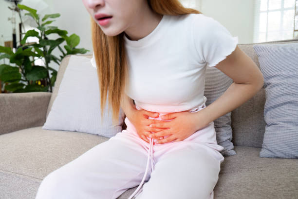 istock A woman is sitting on a couch with a stomach ache 2155995988