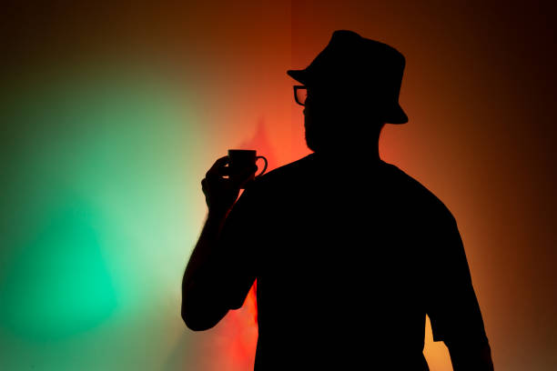 Man in hat in silhouette holding a cup of coffee against colorful background.
