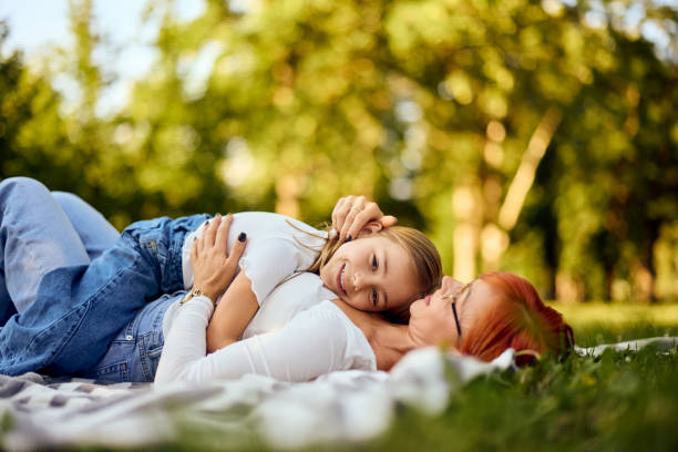 istock Cute smiling daughter lying on her mom while both are lying on a blanket at the park, enjoying the sunny day. 2156006676