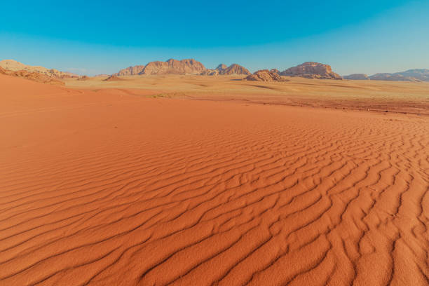 Serene sunset view capturing the textured sands of Wadi Rum, Jordan, with the gentle contours of the landscape leading towards distant mountains under a clear, brightening sky