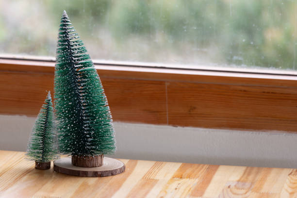 A small Christmas tree sits on a wooden table next to another small tree. The scene is cozy and festive, with the trees adding a touch of holiday cheer to the room