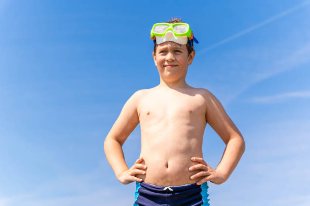 A boy stands on the beach wearing a scuba mask, ready for a swim.