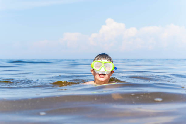A boy swims in the ocean wearing a scuba mask.