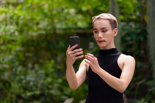 istock Queer LGBT community supporter man with mustache wearing jumpsuit using phone outdoors in park 2156016885