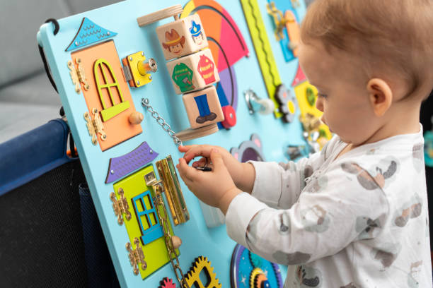 istock Baby holding a key on a chain while playing with a busy board 2156021799