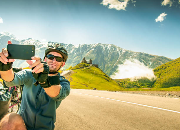 istock Young caucasian cyclist by touring bicycle make self-portrait outdoors while bicycle touring on hilltop viewpoint. Gergeti trinity church. Kazbegi national park 2156028312