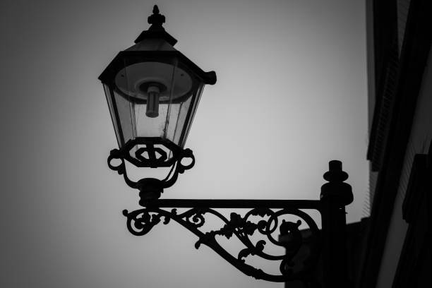 lamp post with a light on it is silhouetted against a cloudy sky in black and white