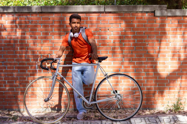 Young man is taking a break from cycling, leaning against a brick wall