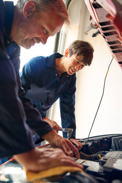 istock Male Car Auto Mechanic With Trainee Under Bonnet Working On Car Engine For Service 2156033843
