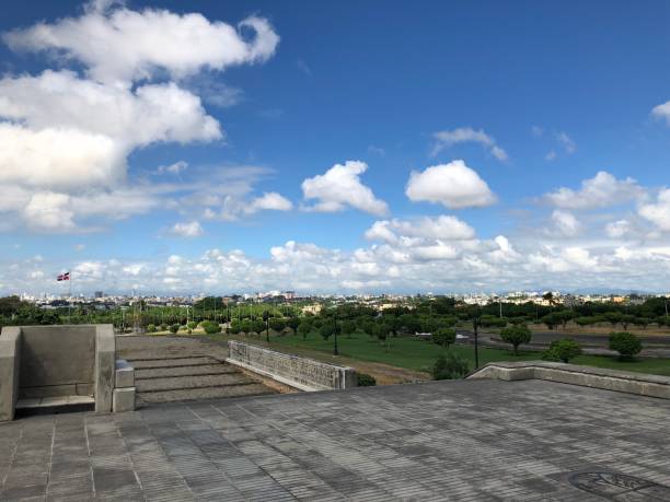istock Grassy field under fluffy clouds with some buildings in Dominican Republic 2156035021