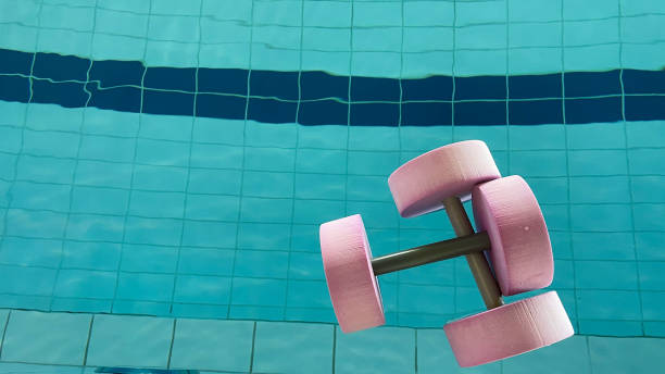 Young adult man smiling, wearing swim goggles and swimming cap, standing on pool stairs, holding onto the handrail after an intense swimming workout in an indoor pool facility