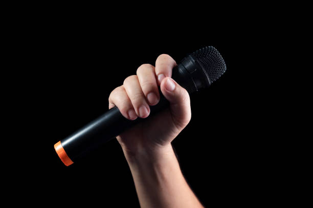 istock black microphone Male singer's hand holding microphone on modern singing stage On a black background and hands 2156043562