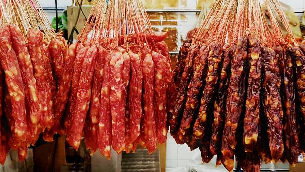 Traditional garlic-flavored halal sausages from Turkey, Turkiye. In Turkish language: Kangal Sucuk or sujuk. A dry, spicy and fermented sausage made from cow or camel meat. Drying homemade raw food hanging on cotton lines in a row at a weekly street market counter. Food background with copy space.