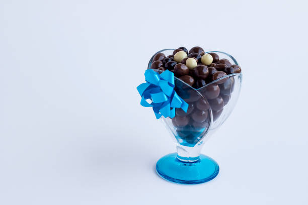 Close-up taken of luxury dark ball chocolates in glass candy bowl at white with blue raffia and copy space.