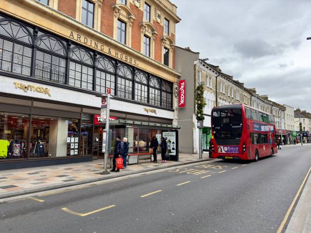 London, United Kingdom – May 06, 2024: Pedestrians passing by storefront with double-decker bus parked