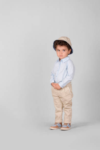 istock little boy standing on a plain white background with light brown pants and a tan hat 2156058473