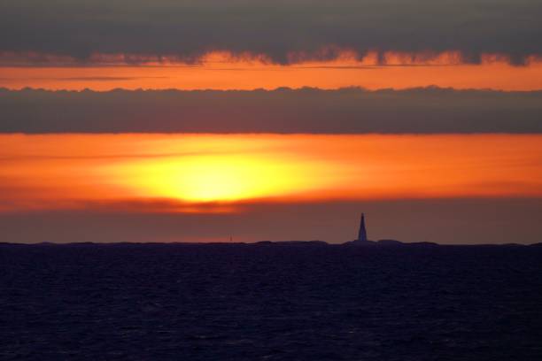 Sun setting behind lighthouse over water and clouds