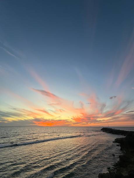istock Dramatic sunset over the ocean with a lighthouse, clouds reflecting in the water 2156062511